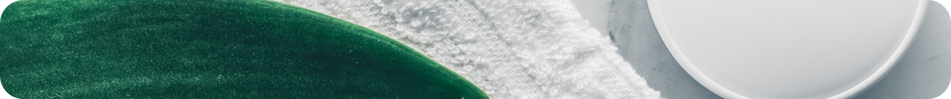 Open jar of cream with a white cap next to a fresh green leaf and a white towel on a marble surface.